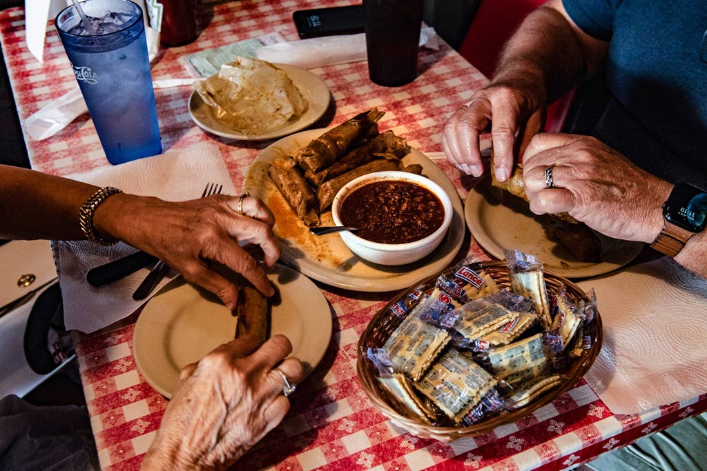 Two people eating hot tamales with chili from Doe's Eatery