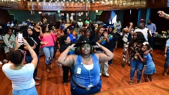 A group of people linedancing in a large room with a stage