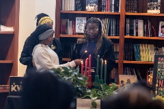 Two Black women watch as a young lady lights the Kinara candles for Kwanzaa
